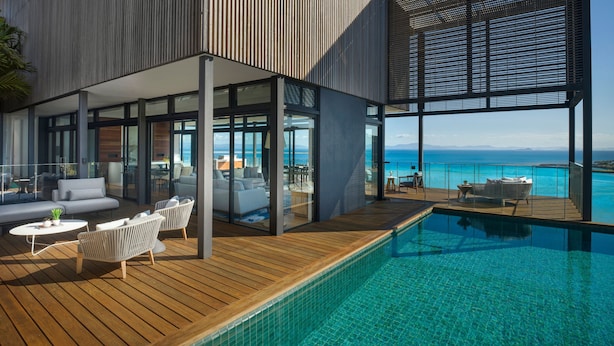Ein moderner Poolbereich im Freien mit einer Holzterrasse, Liegestühlen und Blick auf den Ozean.