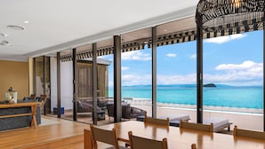Ein moderner Essbereich mit einem großen Tisch, Stühlen, einer Couch und Meerblick durch große Fenster.
