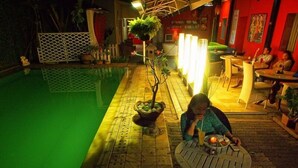 A woman sitting at a table by a poolside, with a dining area and a pool in the background. - Maven Buncit (Jakarta)