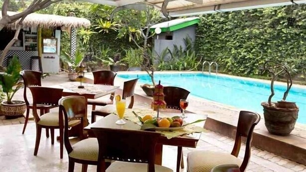 An outdoor dining area with a pool, surrounded by lush greenery and potted plants. - Maven Buncit (Jakarta)