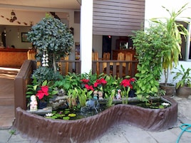 A small outdoor garden area with a pond, potted plants, and decorative statues.