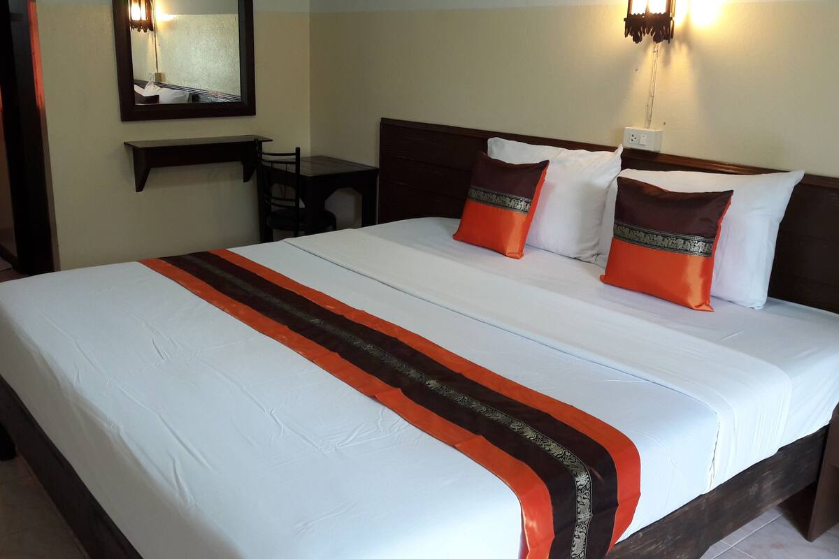 A hotel room with a large bed, a desk, and a mirror.