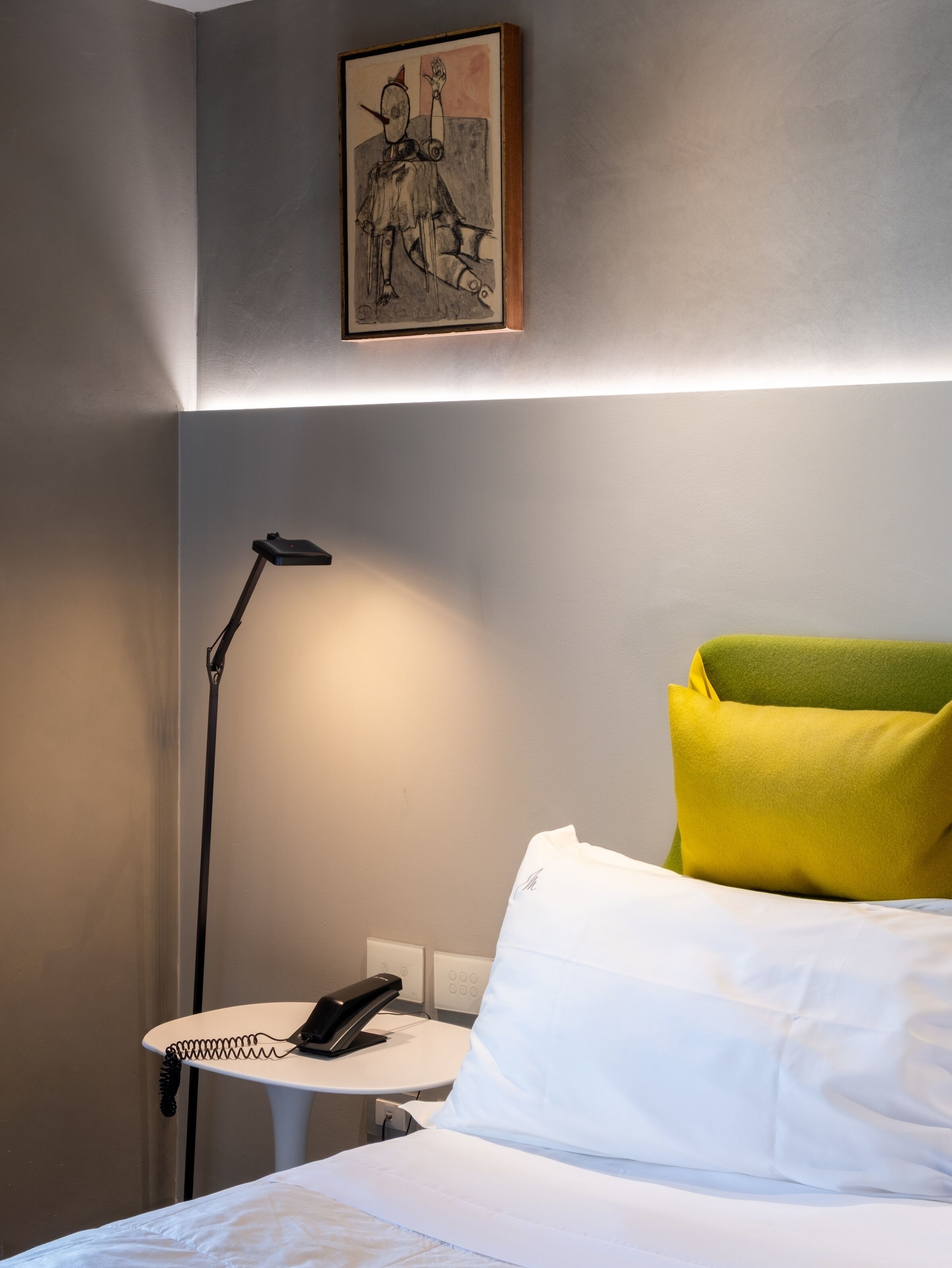 Ein Hotelzimmer mit Bett, Schreibtisch mit Lampe, Telefon und einem Bild an der Wand.