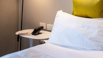 Ein Hotelzimmer mit Bett, Schreibtisch mit Lampe, Telefon und einem Bild an der Wand.