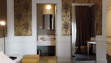 Ein Hotelzimmer mit Bett, Nachttisch, Spiegel, Badezimmer mit Waschbecken und Duschbereich.