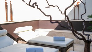 A rooftop lounge area with sun loungers, a decorative tree sculpture, and a white wall with a decorative metal sculpture.