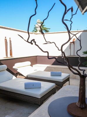 A rooftop lounge area with sun loungers, a decorative tree sculpture, and a white wall with a decorative metal sculpture.