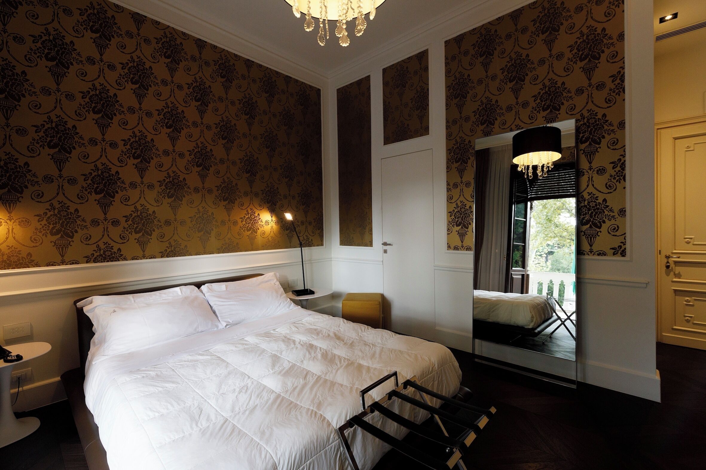 Habitación de hotel con una cama grande, una mesita de noche, una silla, un espejo y vistas al exterior.