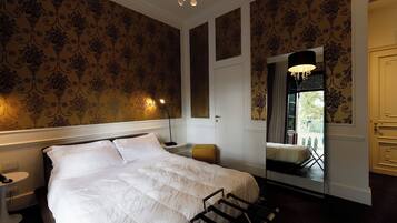 Habitación de hotel con una cama grande, una mesita de noche, una silla, un espejo y vistas al exterior.