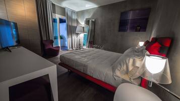 Quarto de hotel moderno com uma cama grande, uma escrivaninha, uma cadeira, uma televisão e uma janela com cortinas.