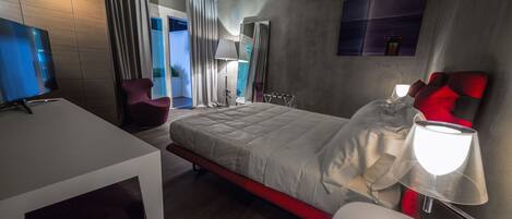 A modern hotel room with a large bed, a desk, a chair, a TV, and a window with curtains.