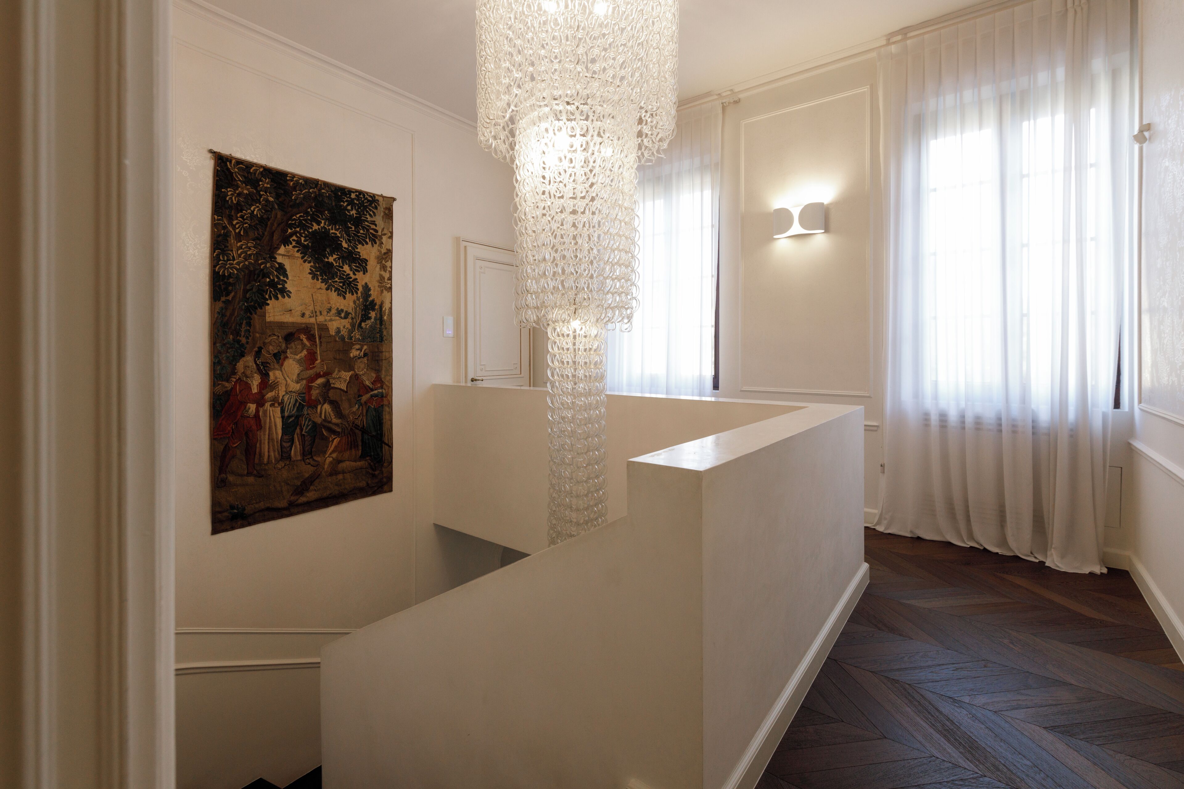 A staircase with a white railing, a decorative chandelier, and a painting on the wall.