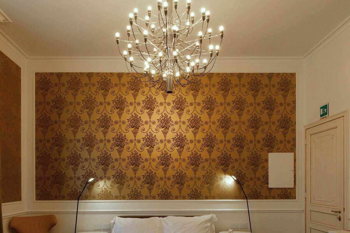 A hotel room with a large bed, a chandelier, a chair, and a small table.