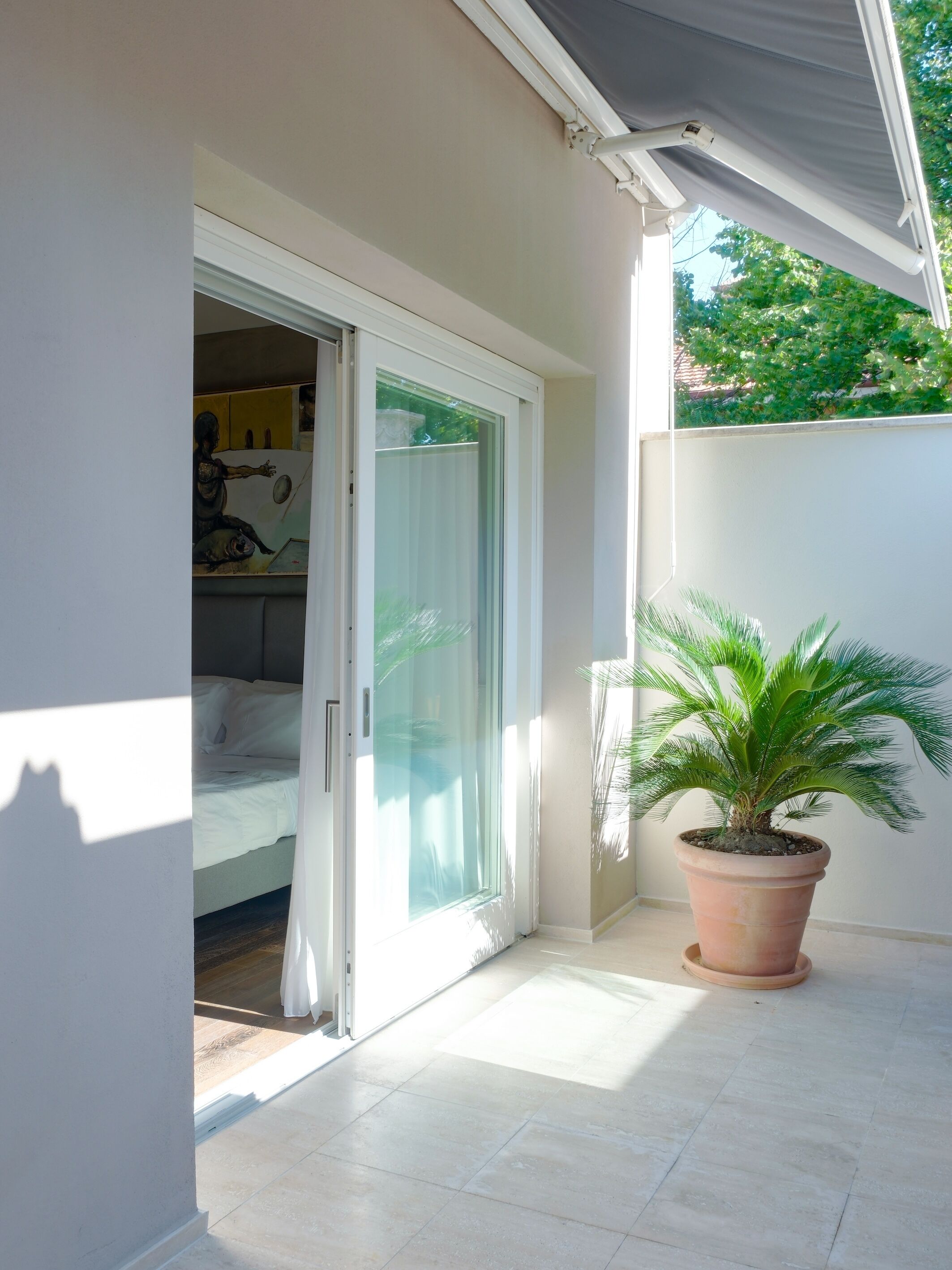 Una habitación con cama, puerta corrediza de vidrio, planta en maceta y piso de baldosas.