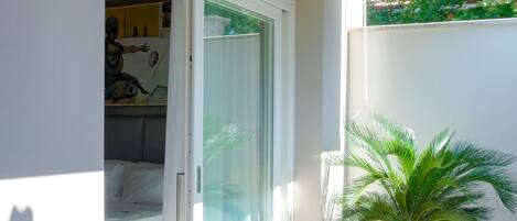 Una habitación con cama, puerta corrediza de vidrio, planta en maceta y piso de baldosas.