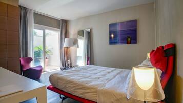 A hotel room with a bed, a desk, a chair, a lamp, a painting, and a window with curtains.