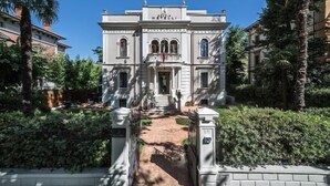 A historic building with a central entrance, flanked by symmetrical wings, and surrounded by lush greenery.