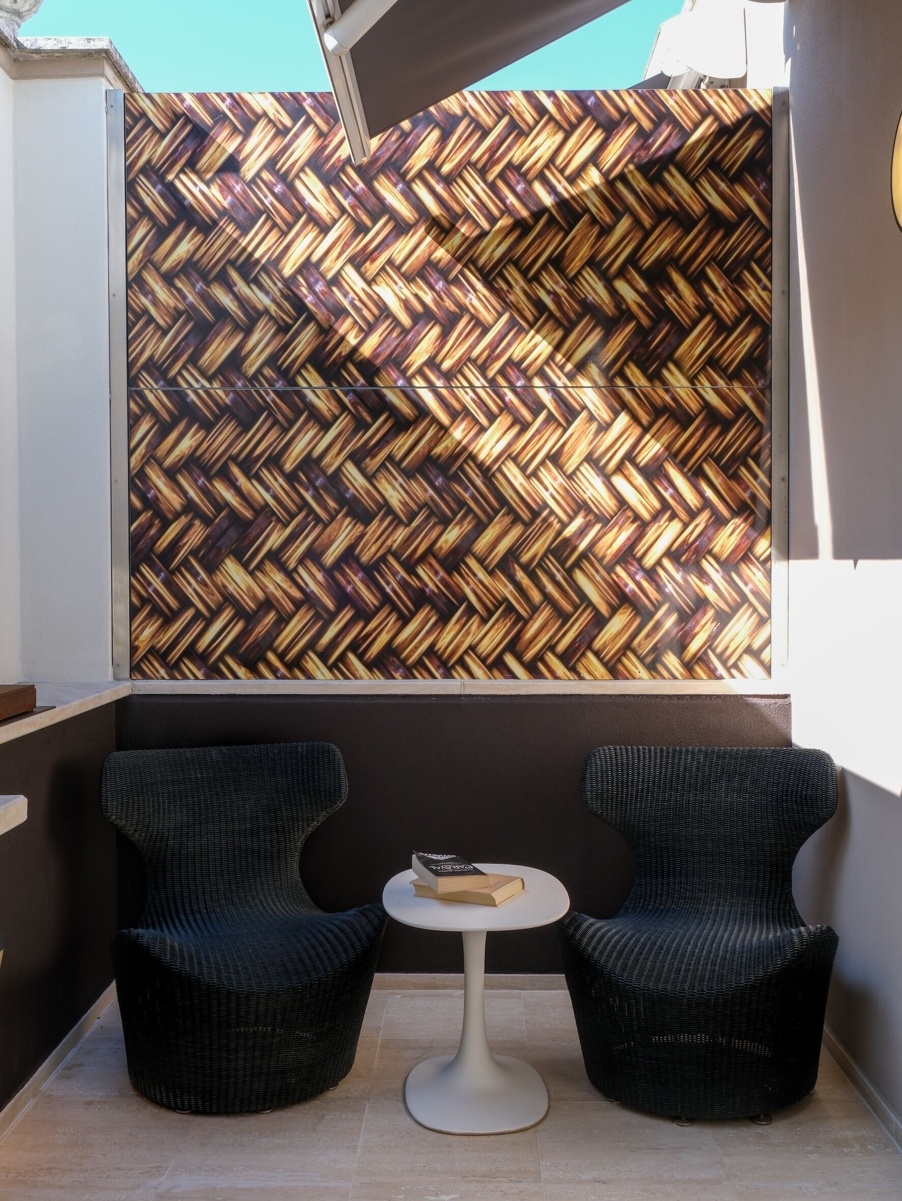 A balcony with two wicker chairs, a small round table, and a woven wall.
