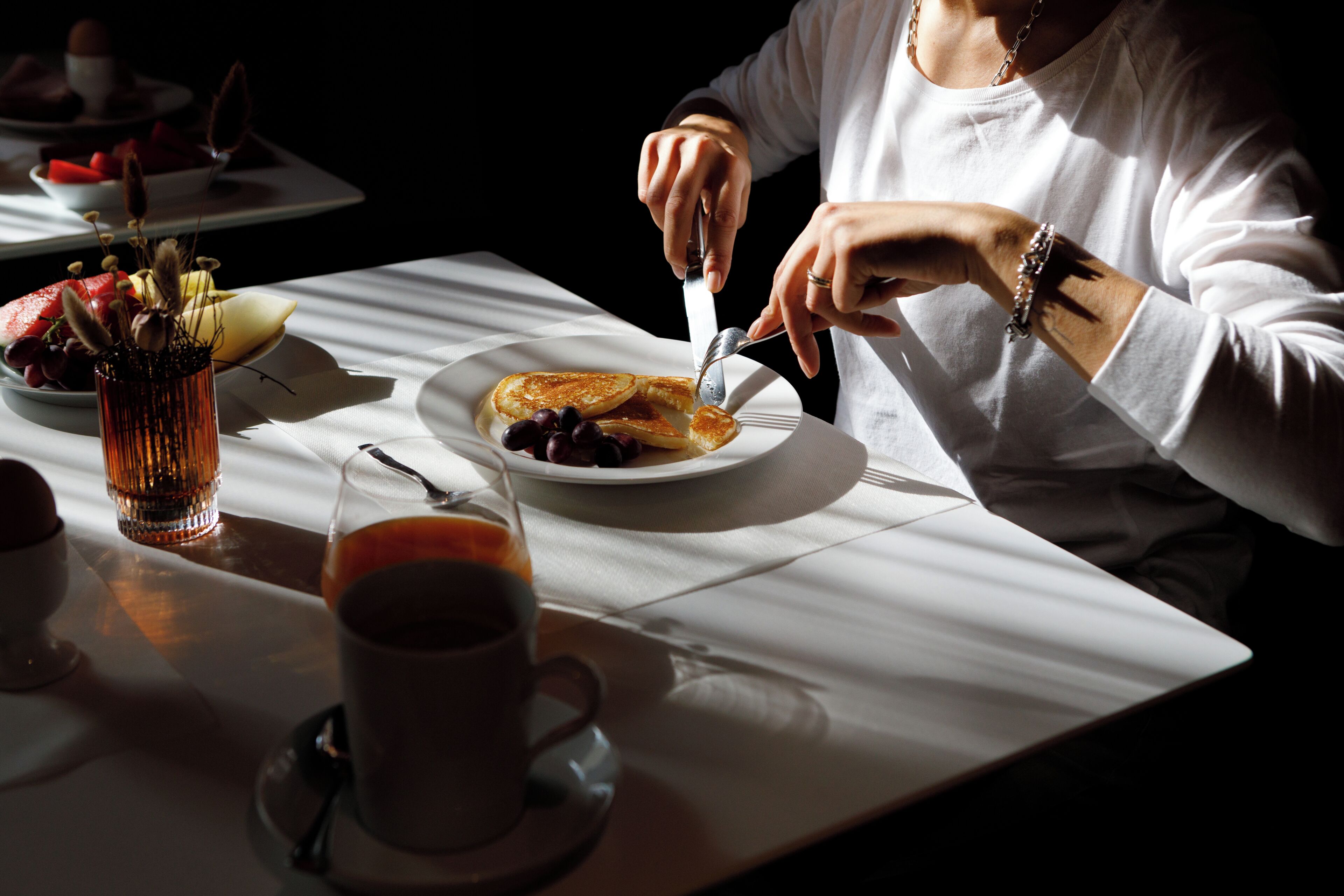 A dining table with a plate of pancakes, a cup of coffee, and a glass of juice.
