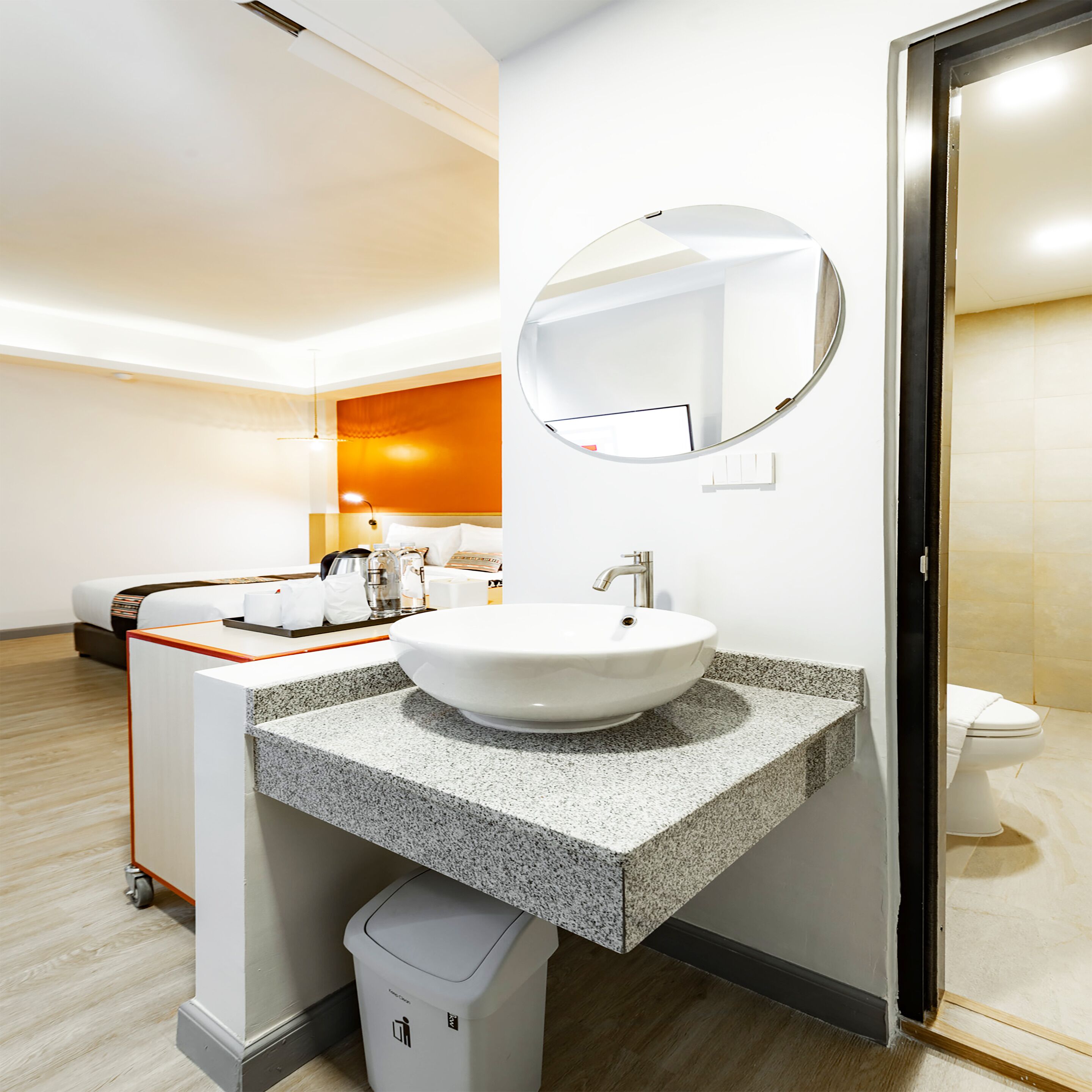 Un baño de hotel con un lavabo blanco, encimera de granito y un espejo redondo.