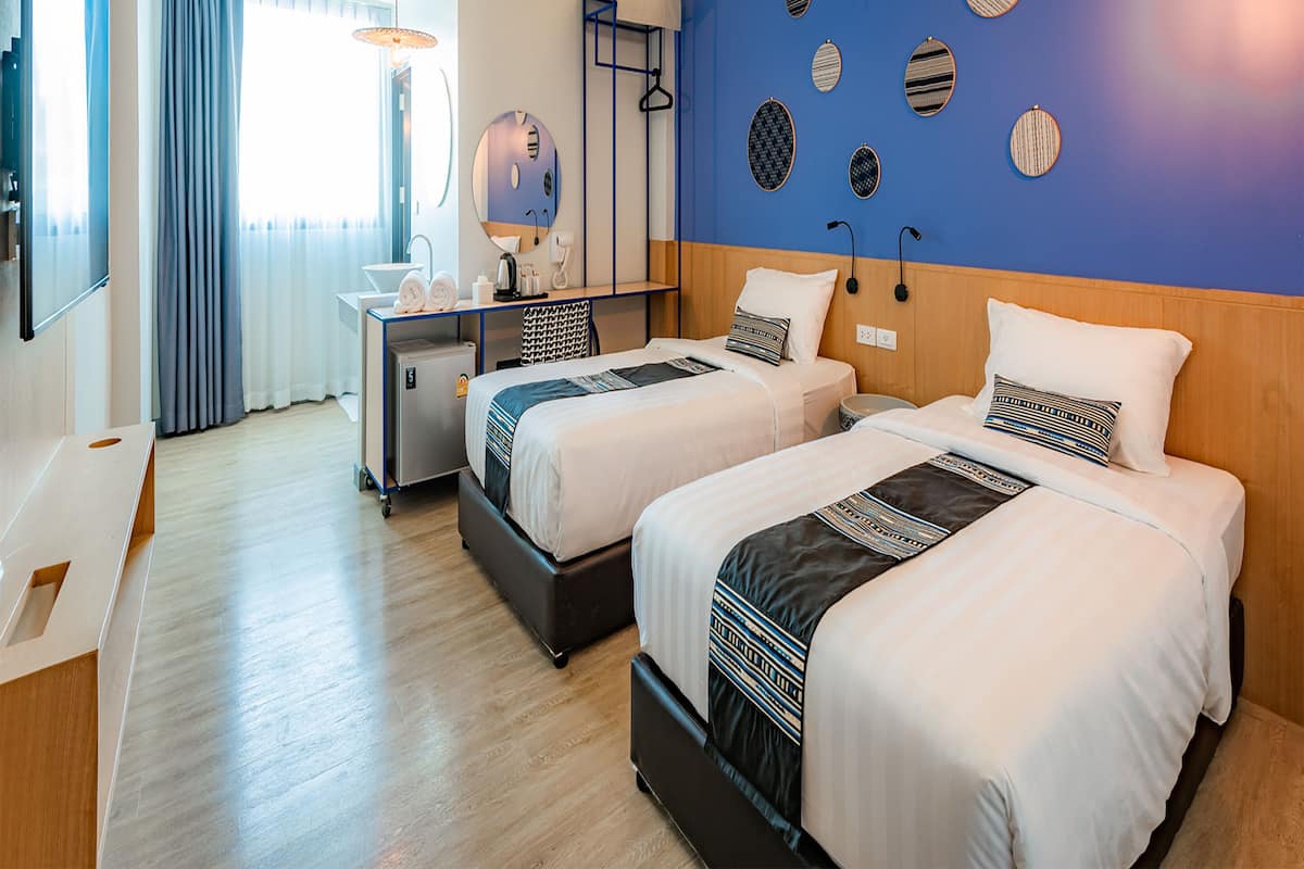 A hotel room with two beds, a desk, a mirror, and a wall with decorative plates.