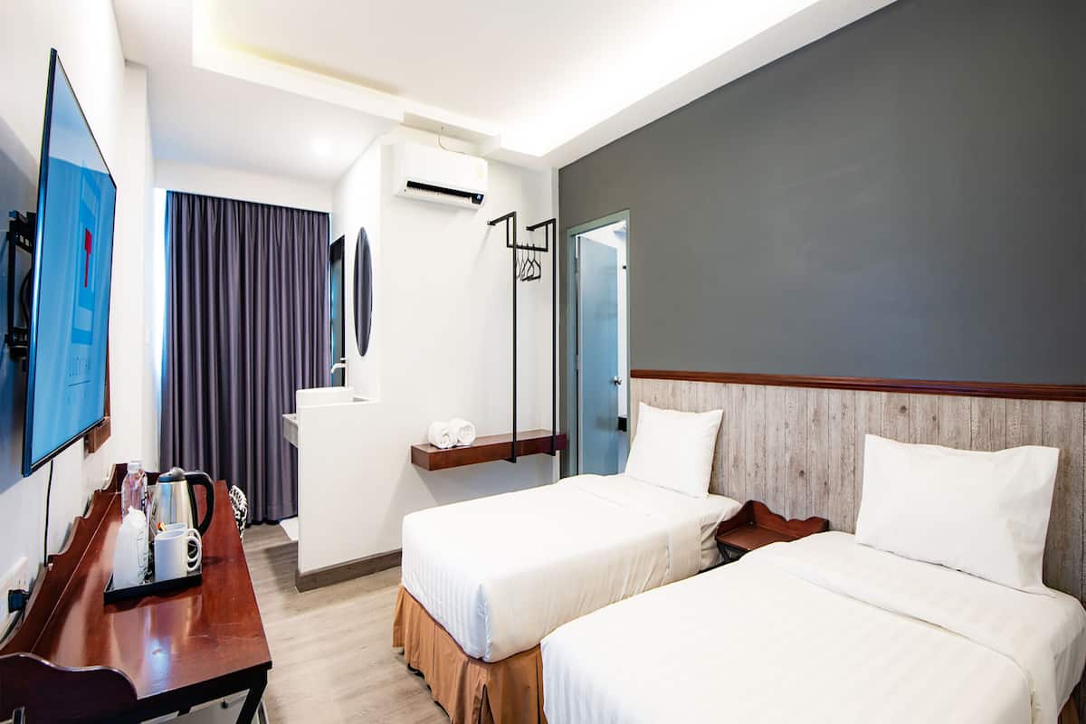 A hotel room with two beds, a desk with a coffee maker, a TV, and a bathroom with a mirror and curtains.