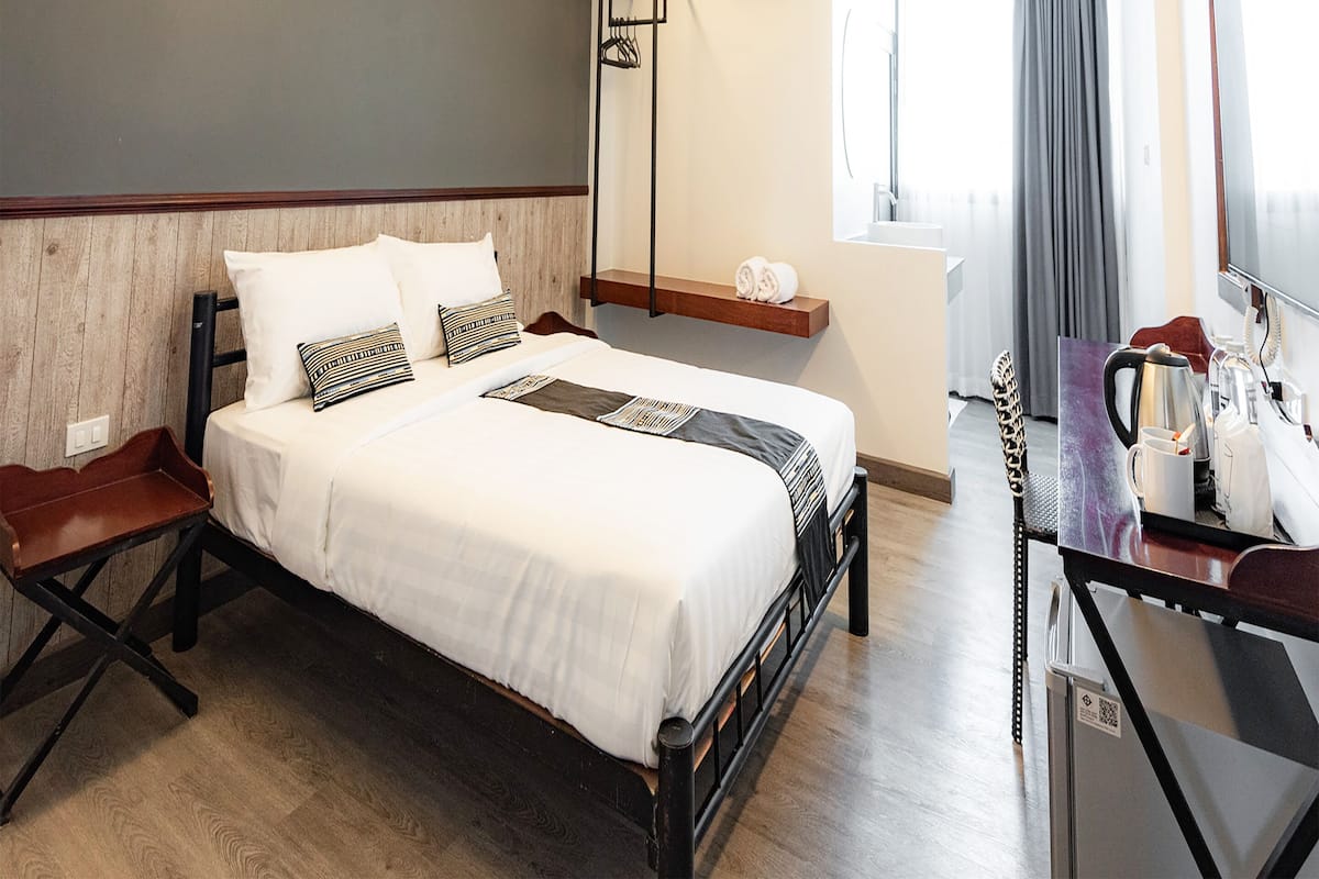 A hotel room with a bed, a desk with a coffee maker, a mirror, and an air conditioning unit.