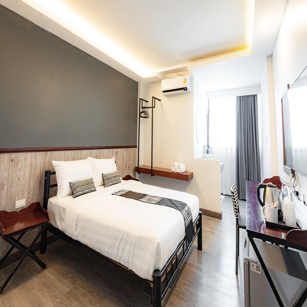 Quarto de hotel com cama, escrivaninha com cafeteira, espelho e ar condicionado.