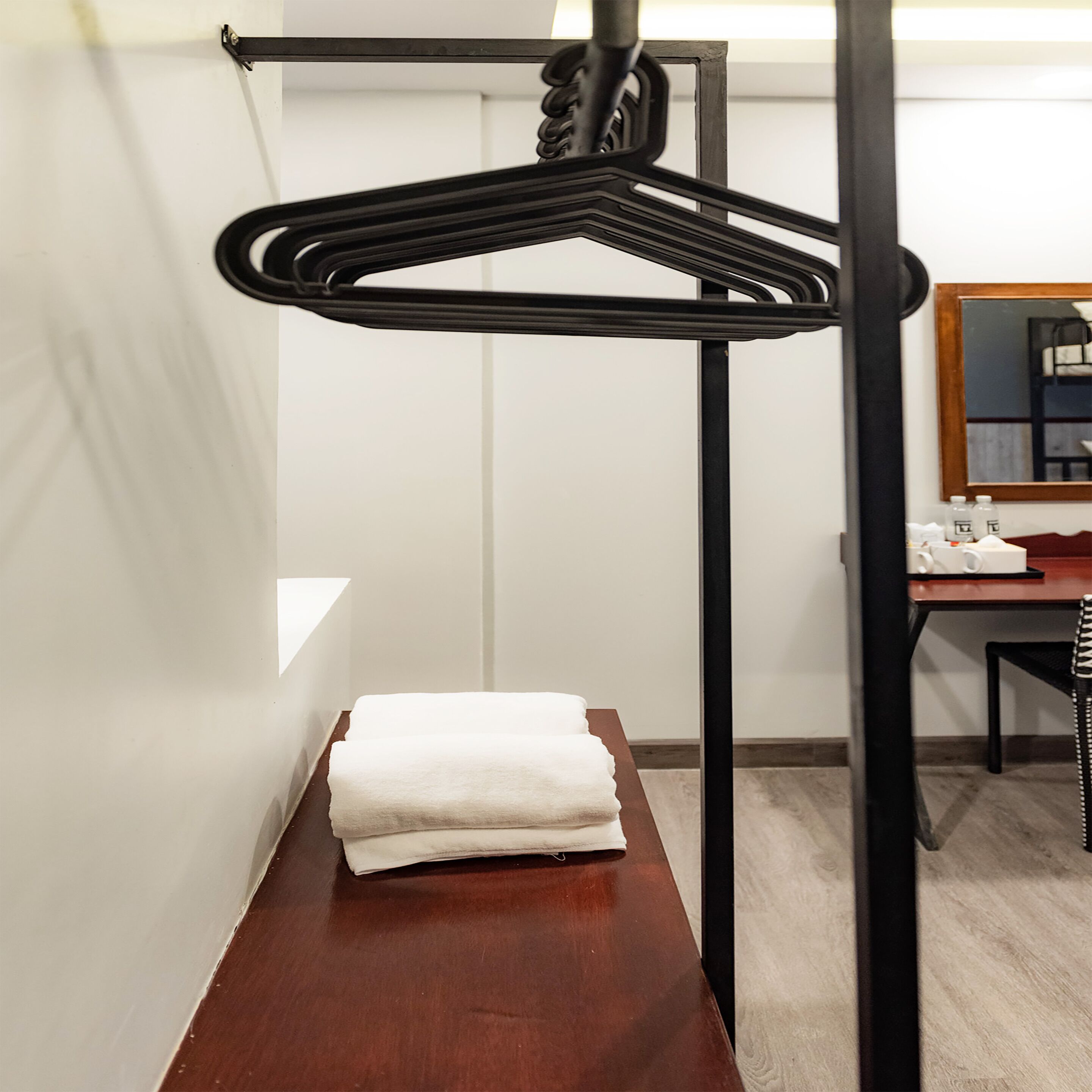 Une chambre d’hôtel avec une table en bois, une serviette blanche pliée, un présentoir en métal noir et un miroir au mur.