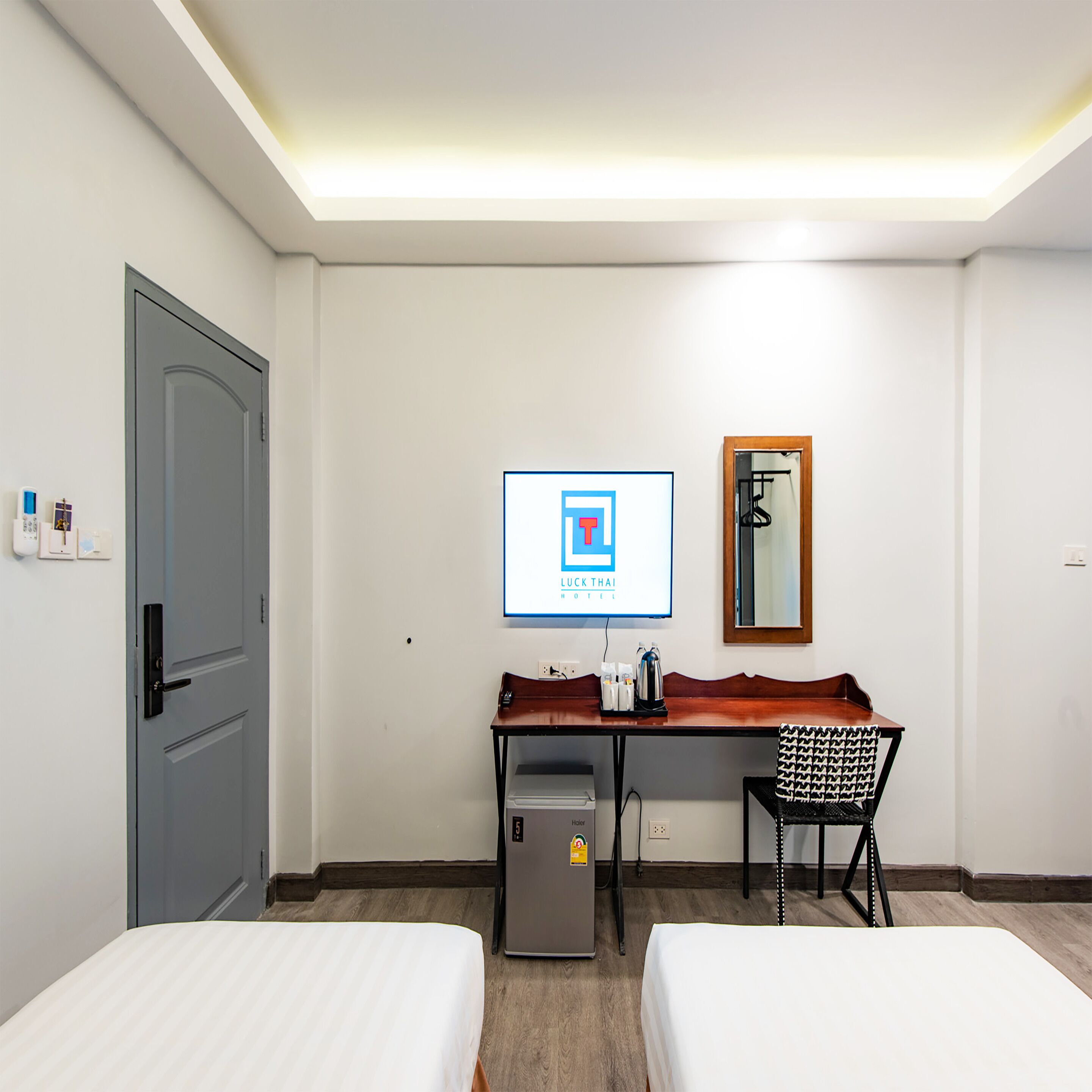 Ein Hotelzimmer mit zwei Betten, einem Schreibtisch, einem Stuhl, einem Kühlschrank, einem Spiegel und einem Schild an der Wand.