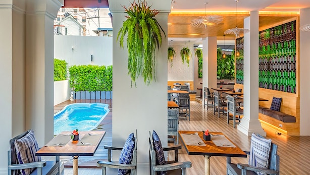 A restaurant with outdoor seating, a pool, and a wall of green bottles. - Luck Thai Hotel (Chiang Mai)