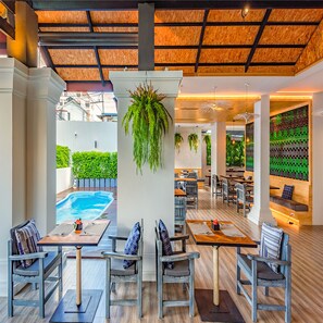 Restaurante com área externa, piscina e parede de garrafas verdes.