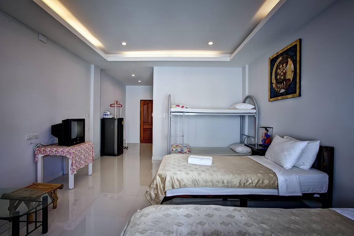 A hotel room with a bunk bed, a desk with a television, a small table, and a painting on the wall.