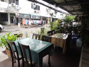 An outdoor seating area with tables and chairs, surrounded by potted plants and a view of a street with shops and hanging laundry. - Misone Hotel (Chiang Mai)