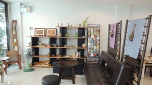 A modern living room with a sofa, a coffee table, and a fan. There are shelves with books and decorative items. - Misone Hotel (Chiang Mai)