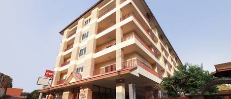 A multi-story hotel with a central entrance, balconies on each floor, and a sign indicating the name.