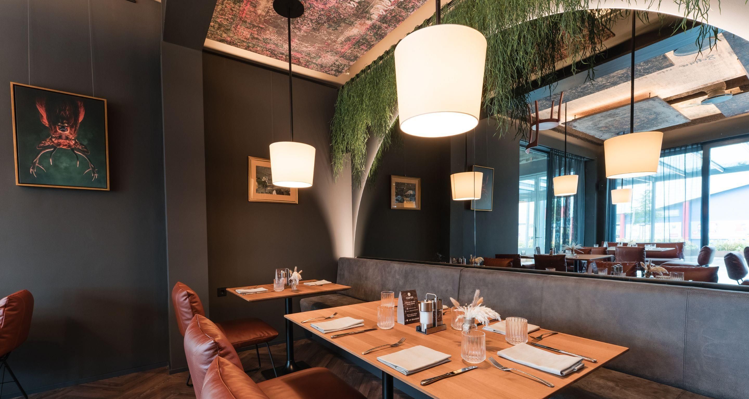 A restaurant interior with wooden tables, leather chairs, pendant lighting, and a large mirror reflecting the room.