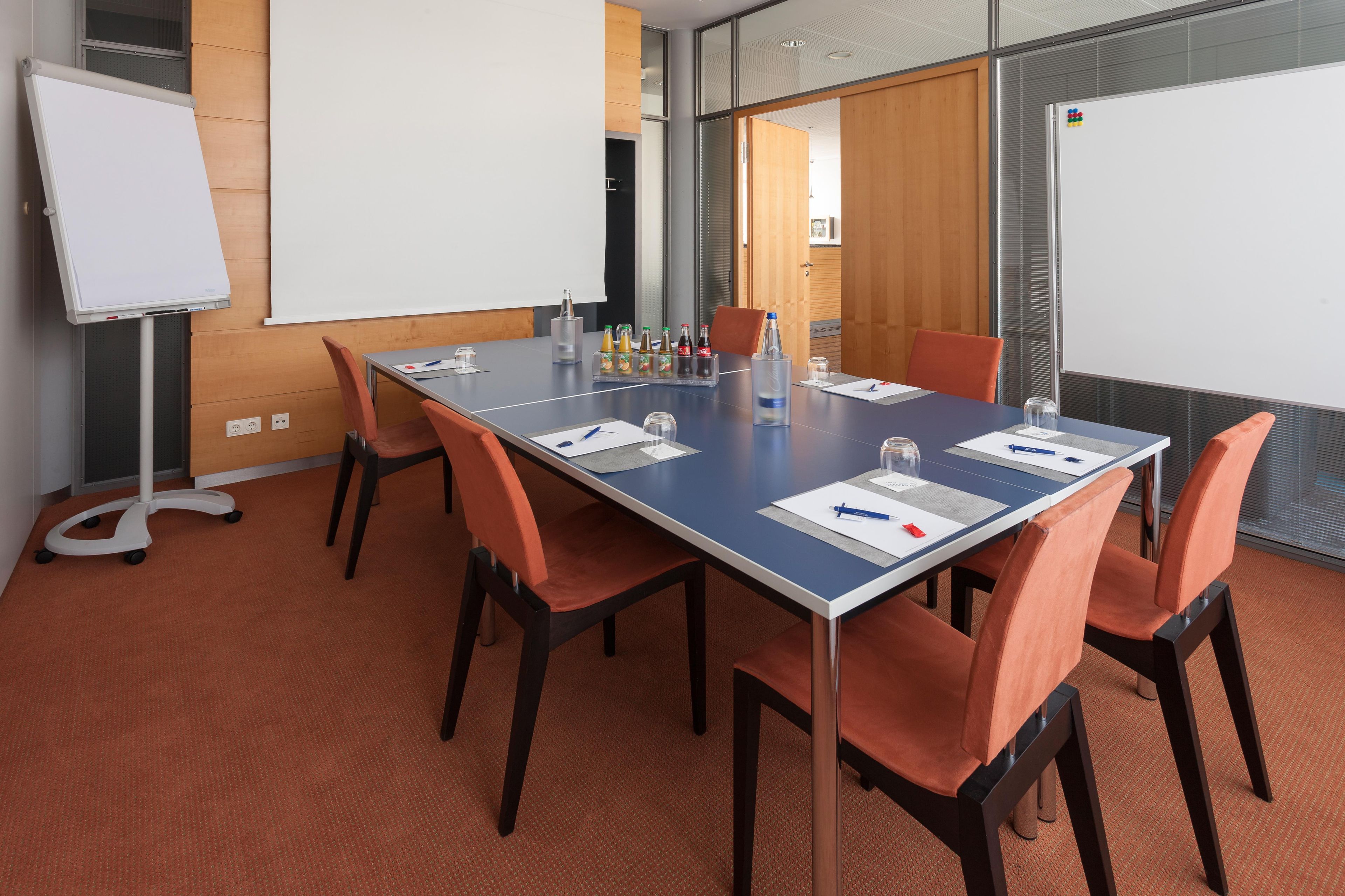 Un salón de conferencias con una mesa larga, sillas, una pizarra y un panel de vidrio.