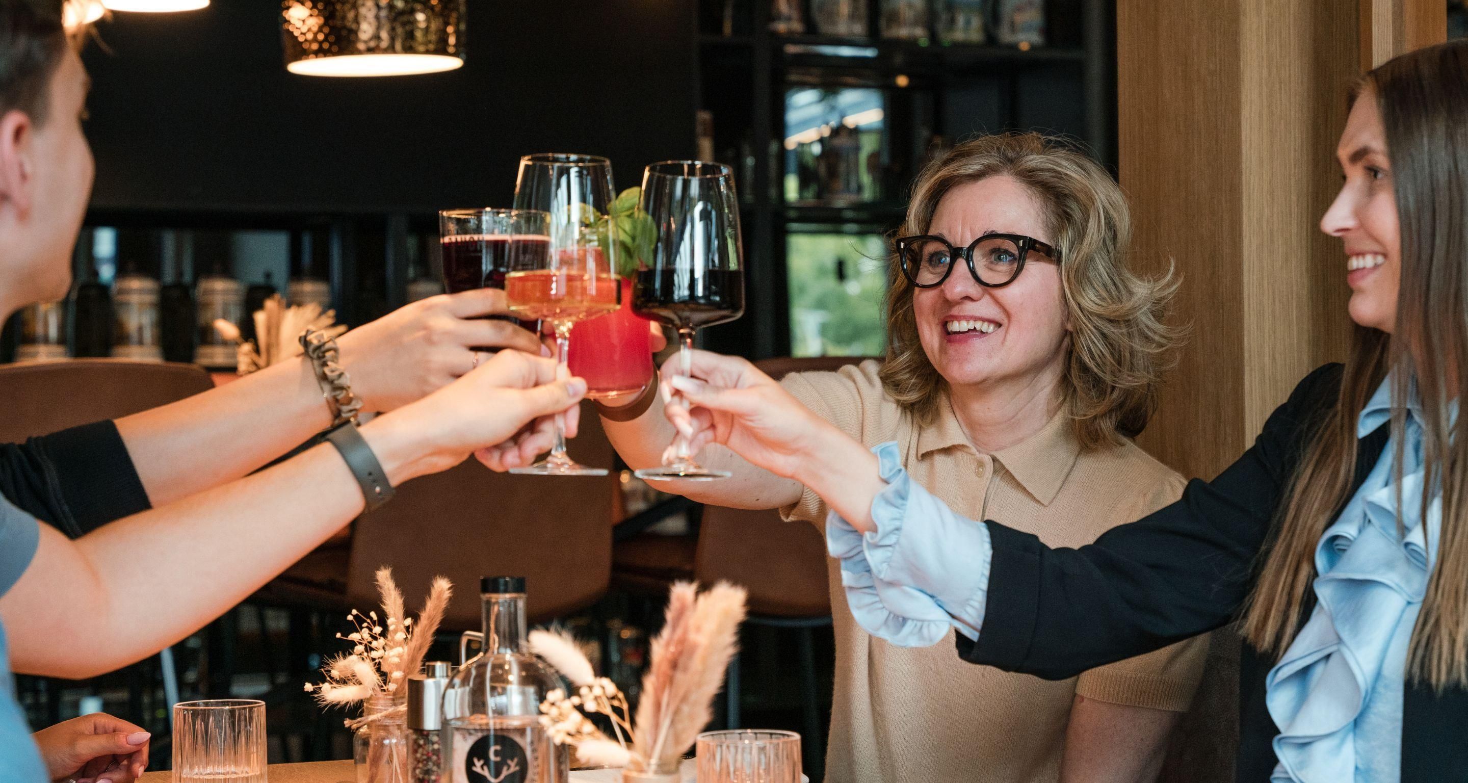A group of people toasting with drinks at a table with a bottle and glasses.