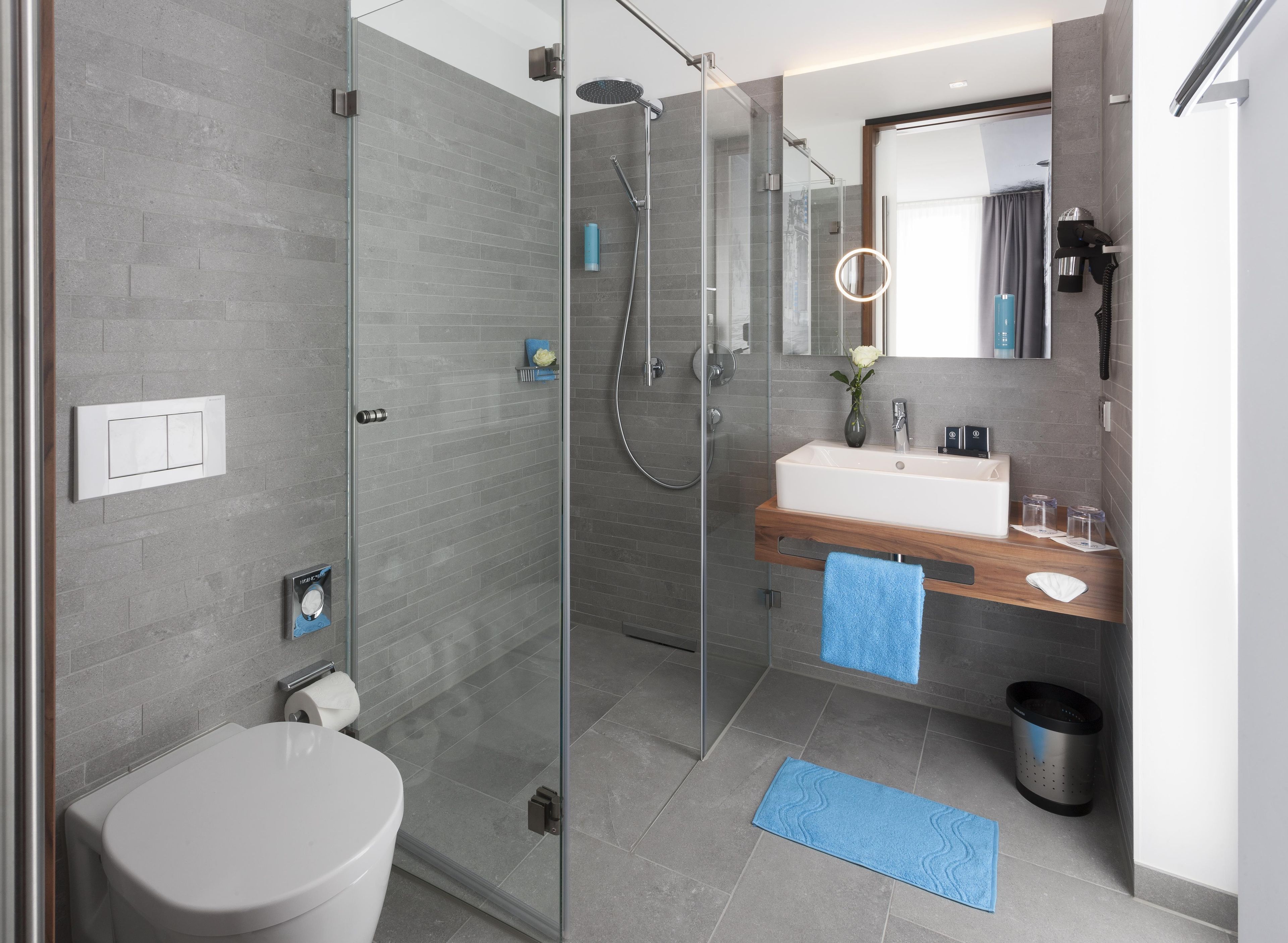 Ein modernes Badezimmer mit einer gläsernen Dusche, einem weißen Waschbecken und einem Spiegel darüber.