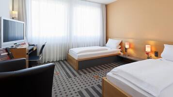Habitación de hotel con cama, escritorio, computadora, televisor y una silla.
