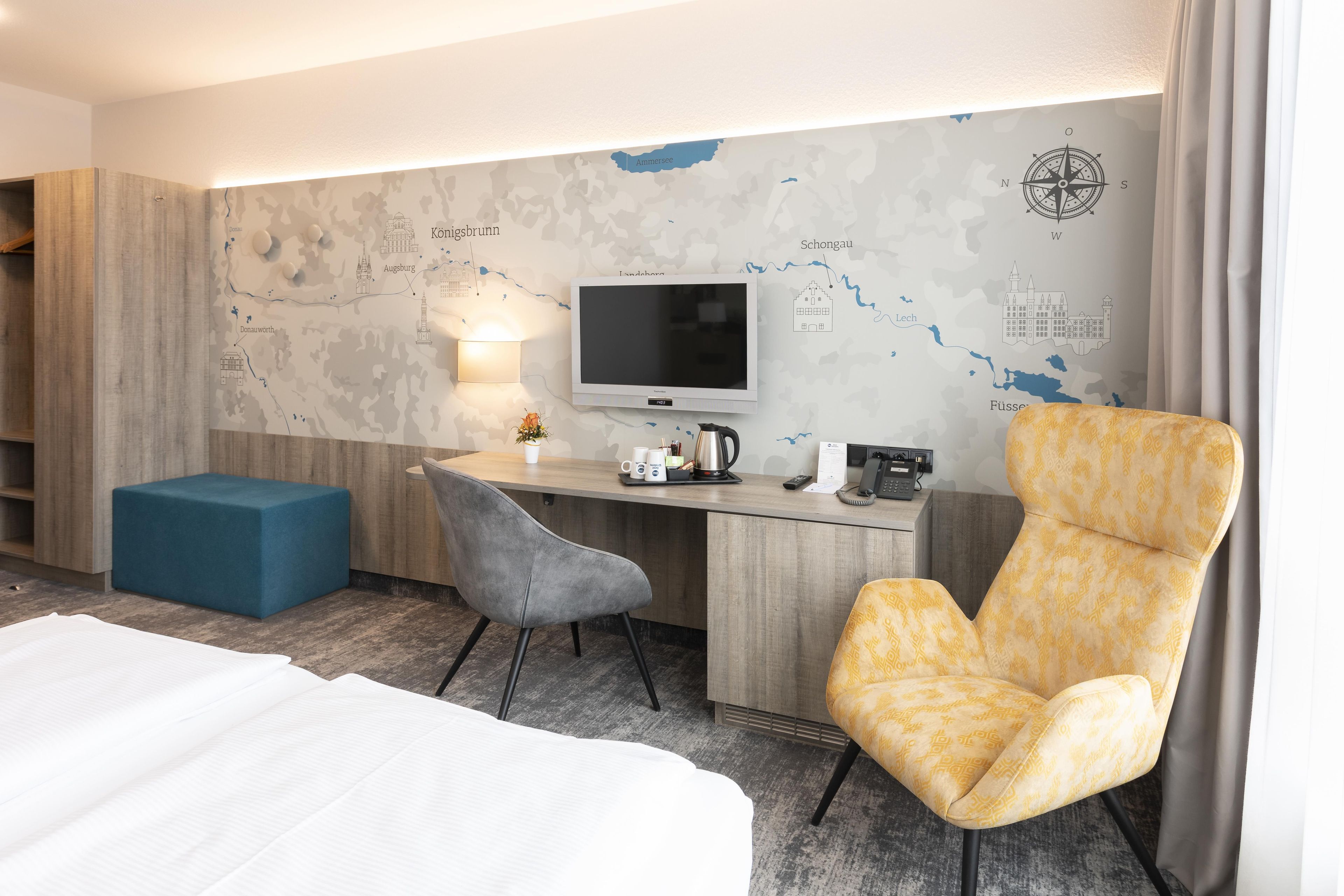 Una habitación de hotel con una cama, un escritorio con una computadora, una silla y un mapa en la pared.