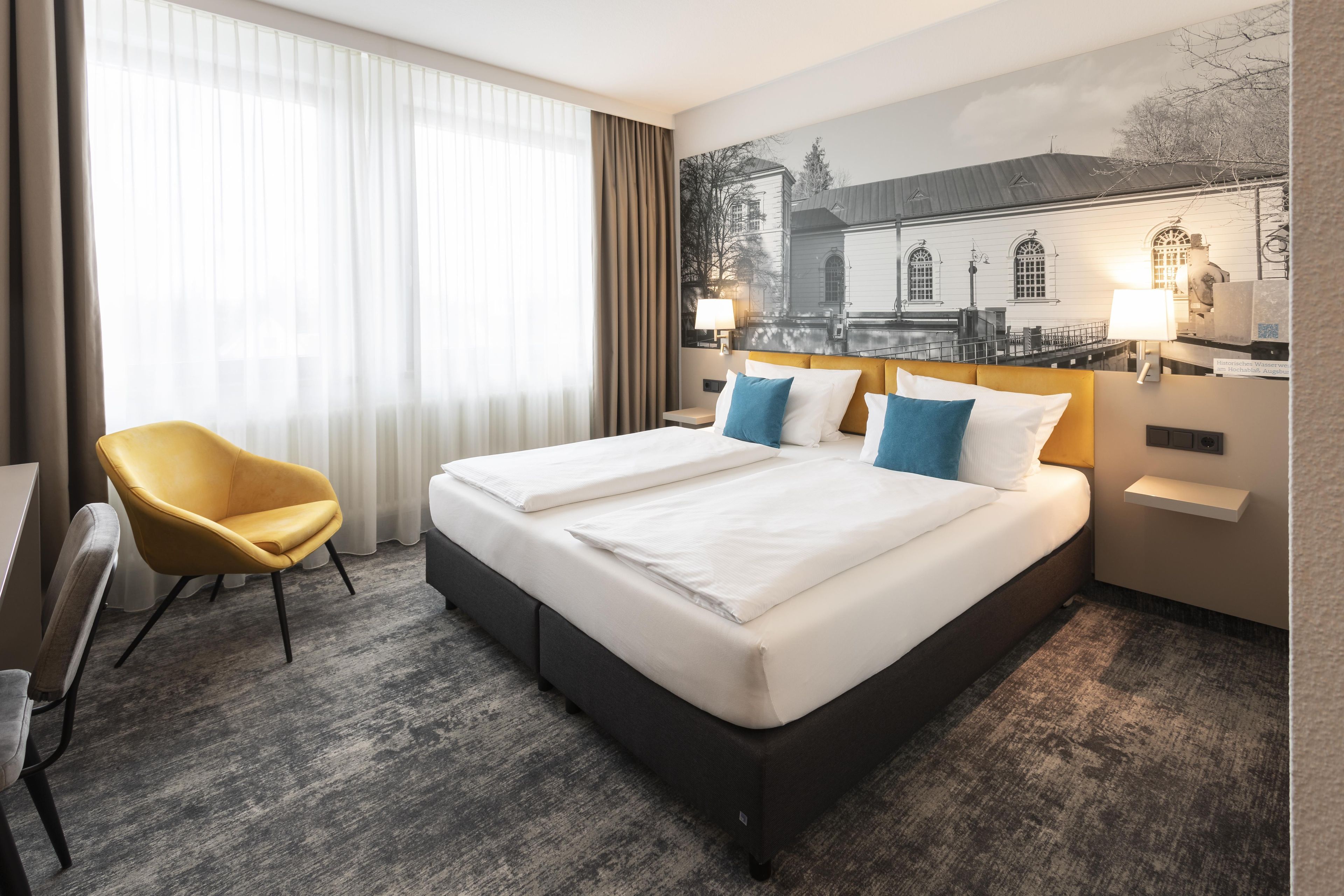 A hotel room with a large bed, two bedside tables, a chair, and a view of a building through the window.