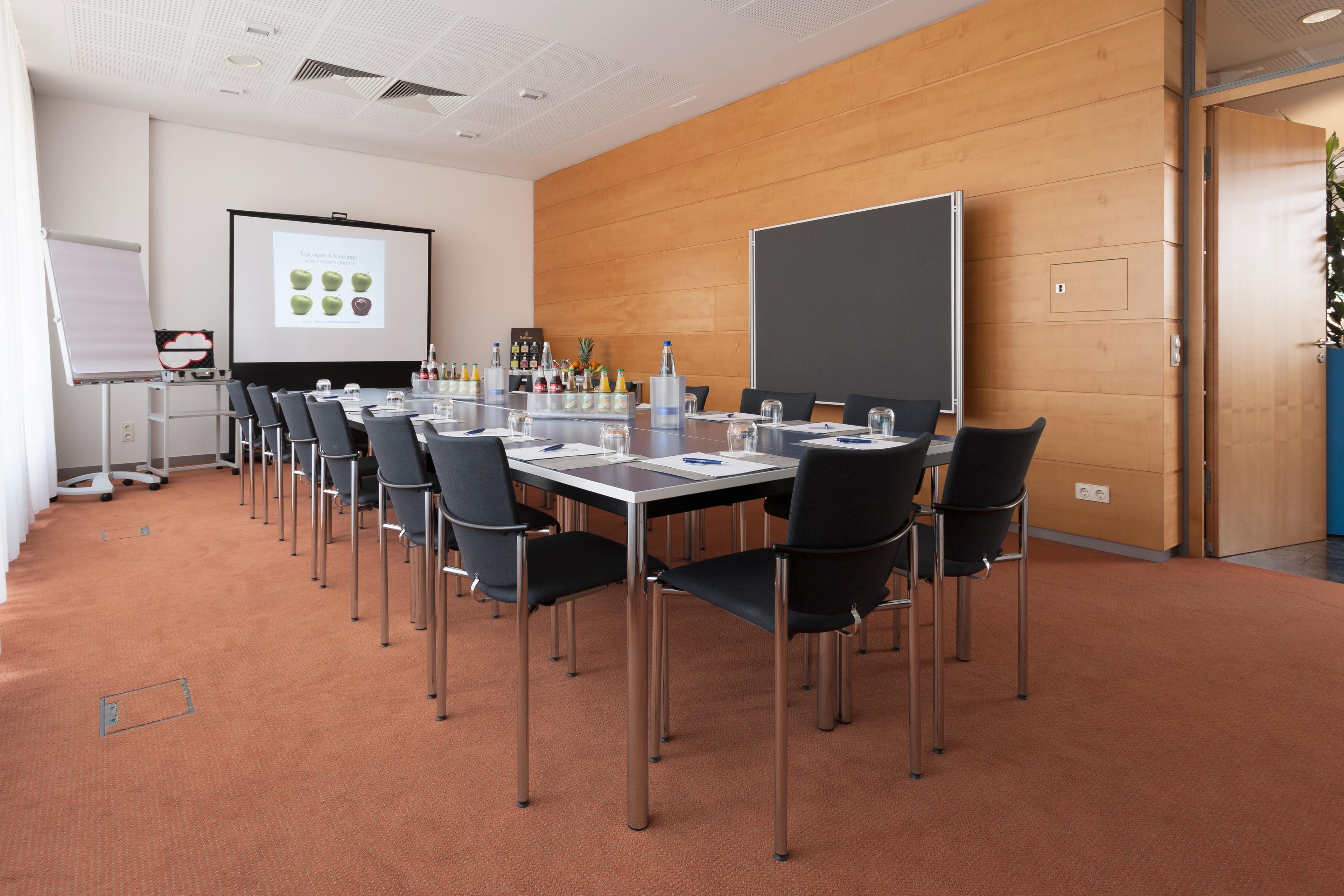 A conference room with a long table, chairs, a projector screen, and a presentation on the wall.