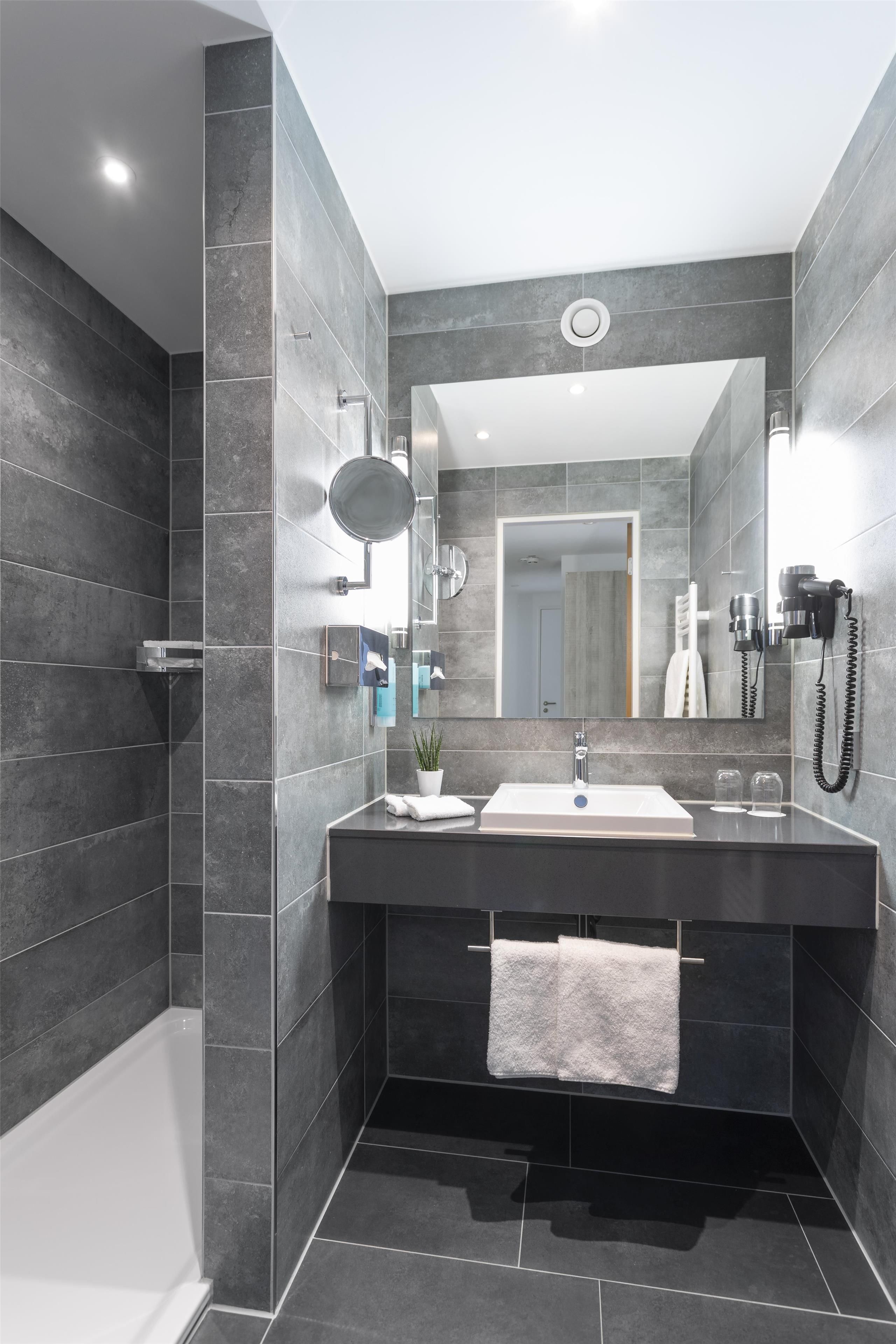 Une salle de bain moderne avec un grand miroir, un lavabo et une douche.
