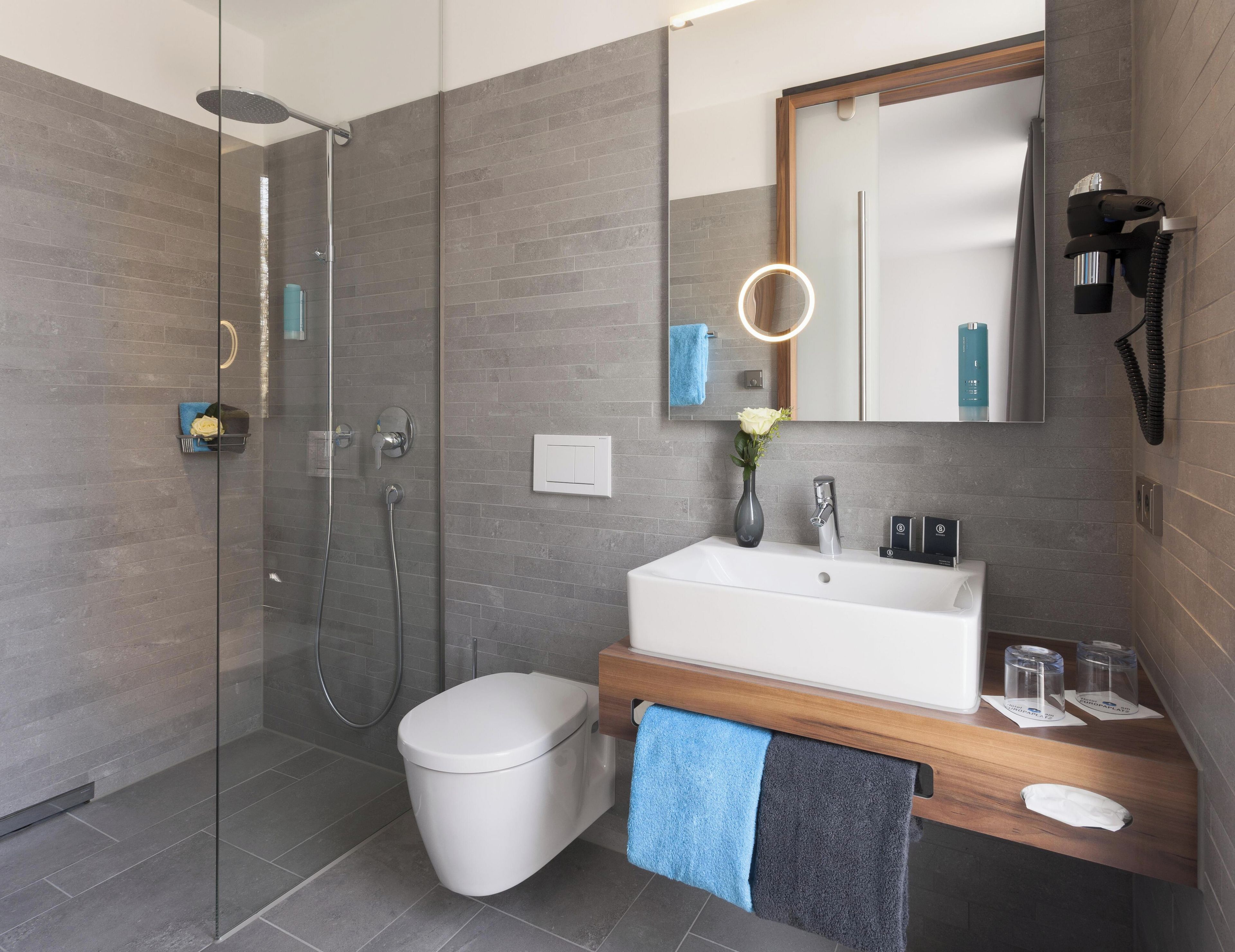 A modern bathroom with a glass-enclosed shower, a white toilet, a vanity with a mirror, and a towel rack.