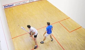 Una cancha de squash con suelo de madera y líneas divisorias anaranjadas.