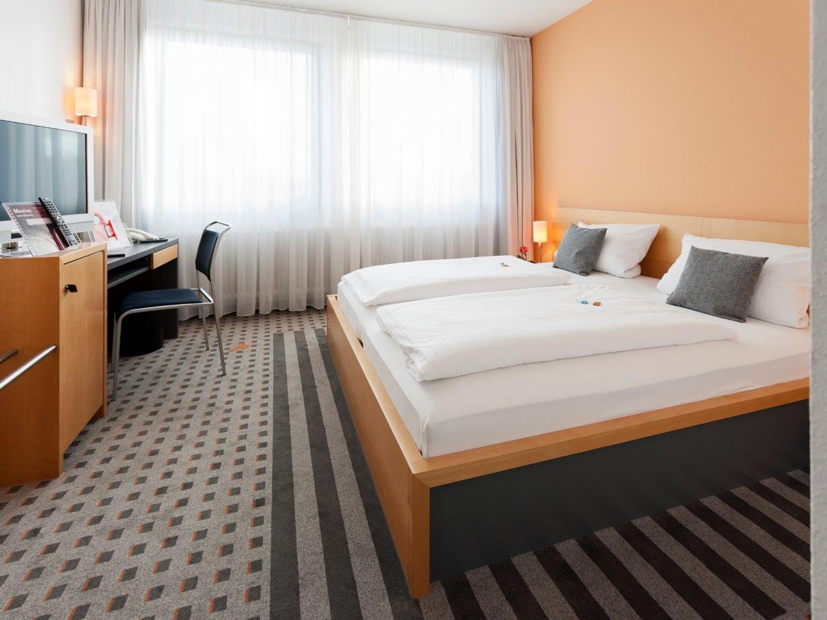 A hotel room with a large bed, a desk, a chair, and a television.