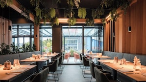 Un restaurante moderno con mesas largas, sillas negras y plantas colgantes.