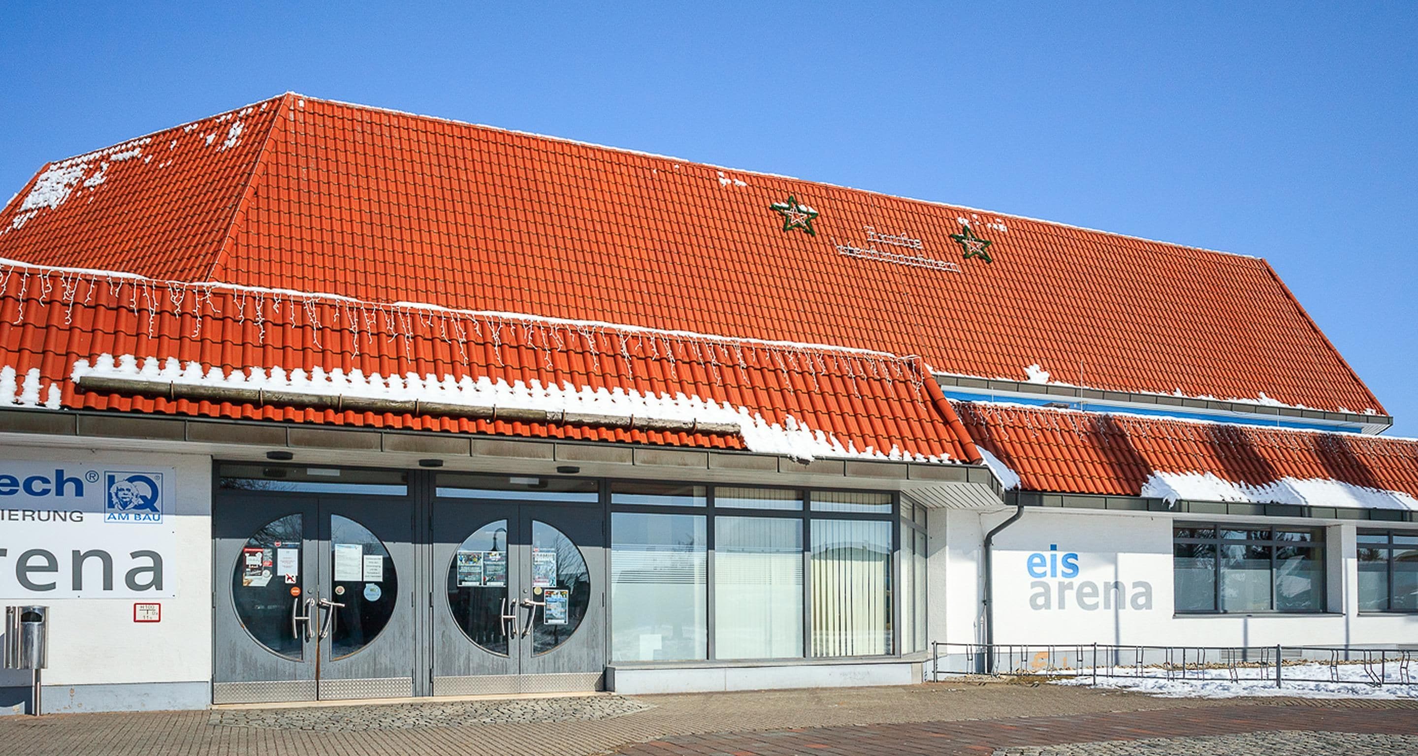 A building with a red-tiled roof, large windows, and signage for 'eis arena.'